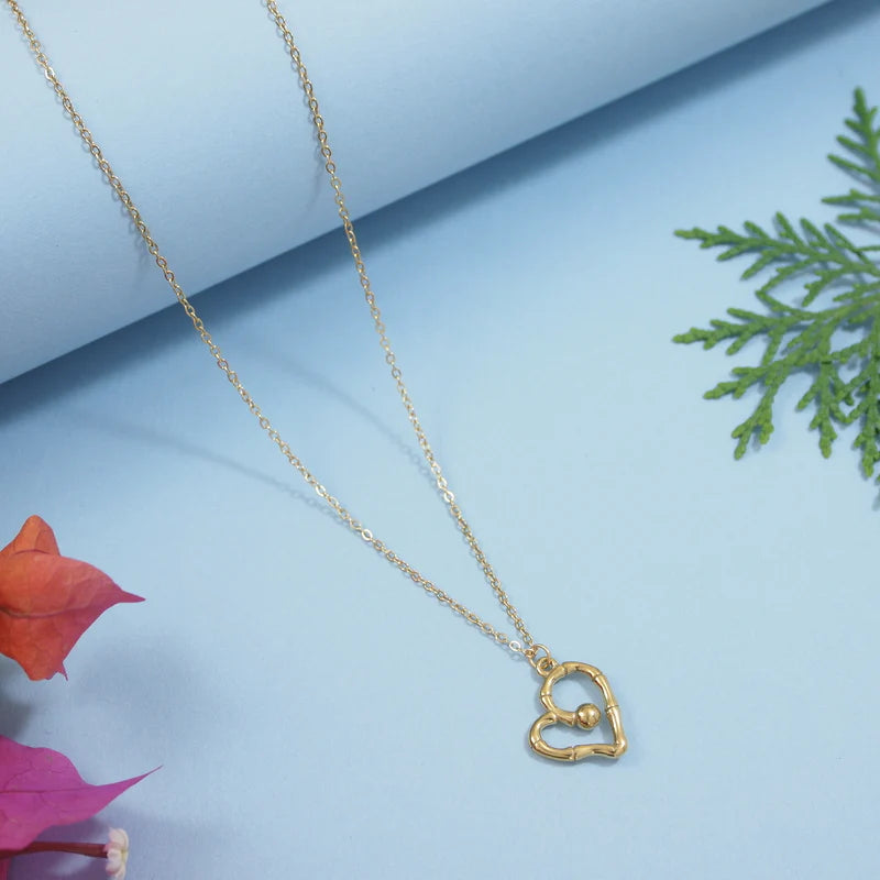 Gold heart-shaped necklace on a light blue background with pink leaves and greenery.