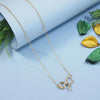 Gold necklace with a decorative pendant on a light blue surface with green leaves.