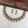 Gold necklace with green and red stones and matching earrings on a white surface with a wooden box in the background.
