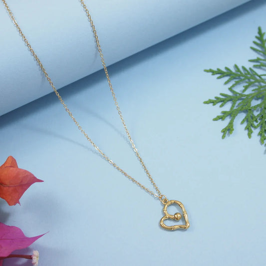 Gold heart-shaped necklace on a light blue background with pink leaves and greenery.