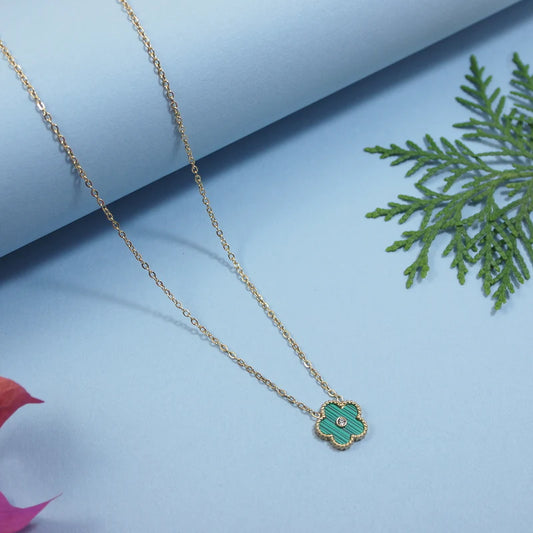 Gold necklace with a green pendant on a light blue background with green leaves.