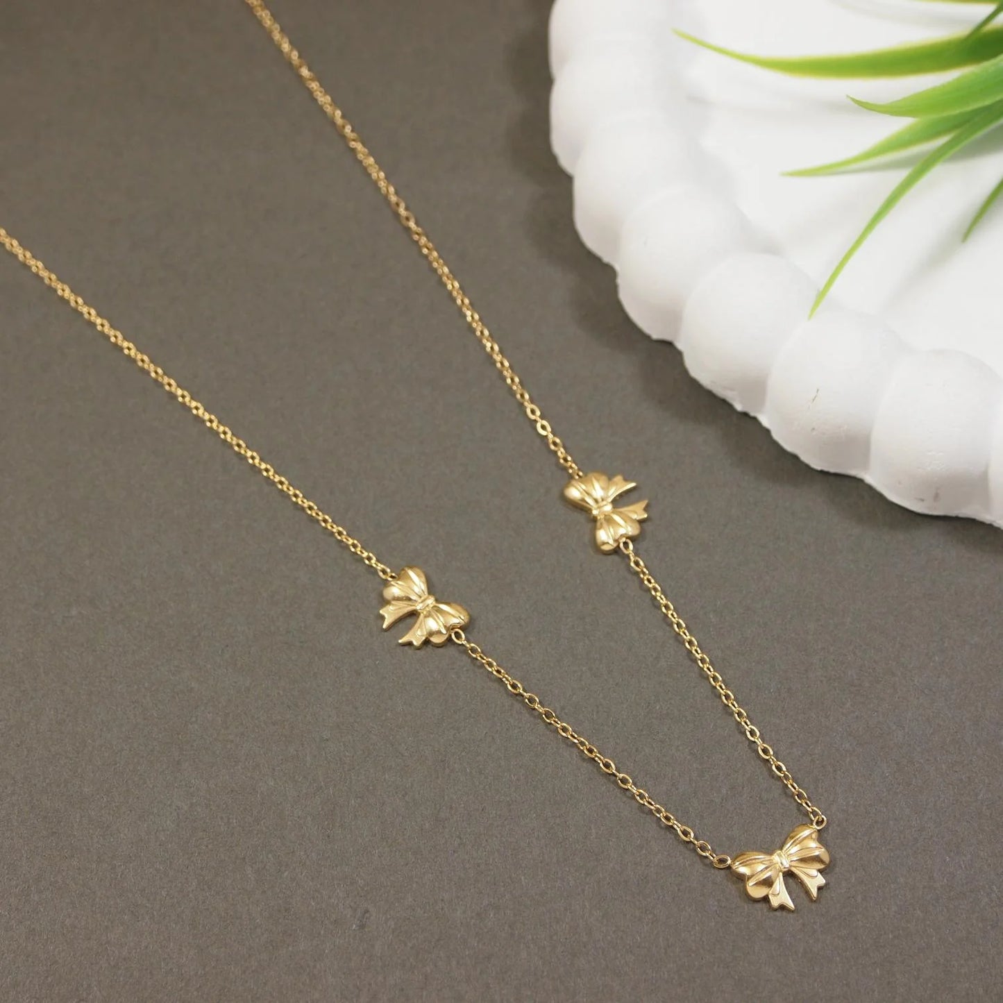 Gold necklace with bow pendants on a gray surface